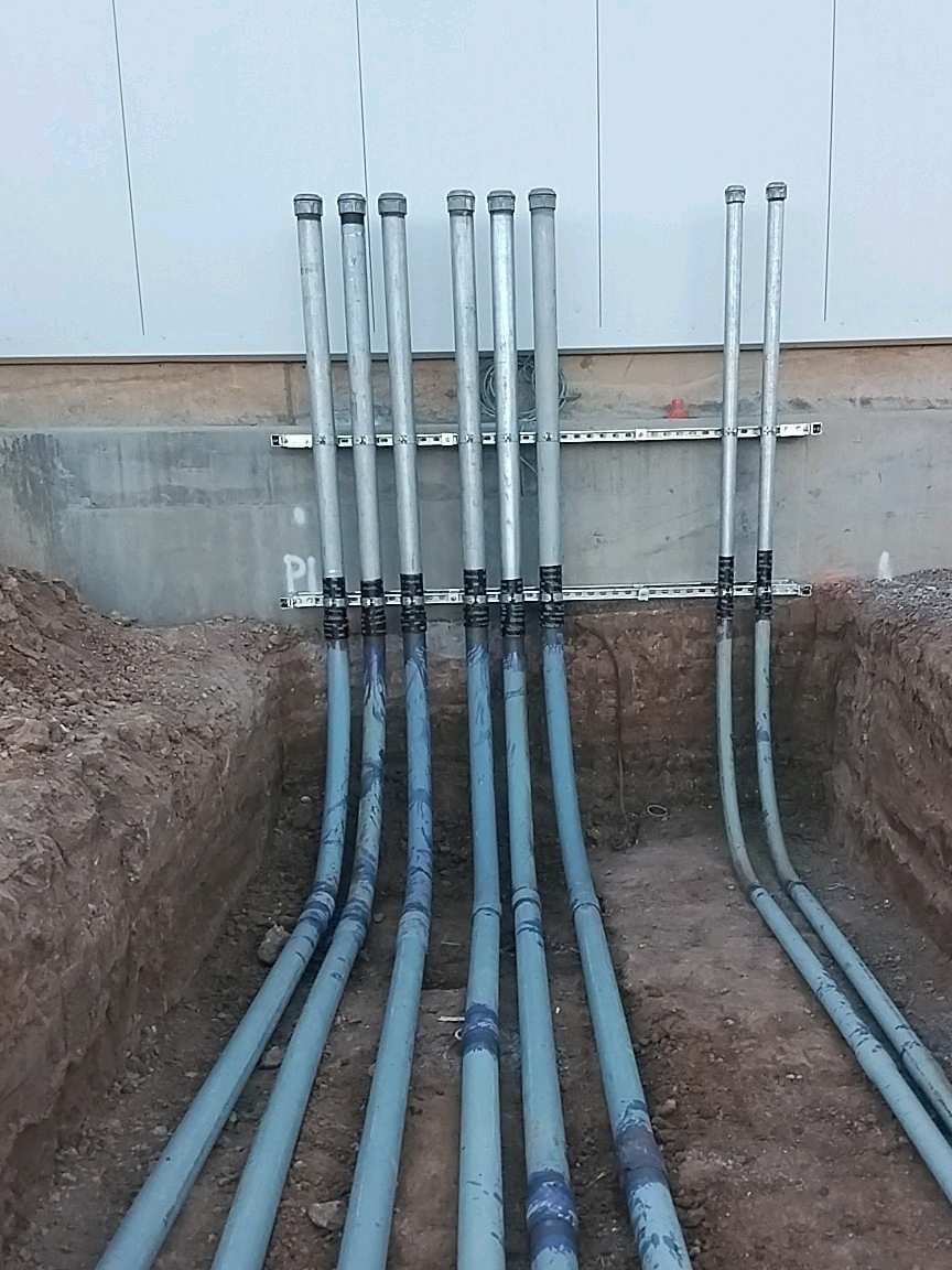 A bank of conduit stubbed up and strapped to the building wall, before backfill