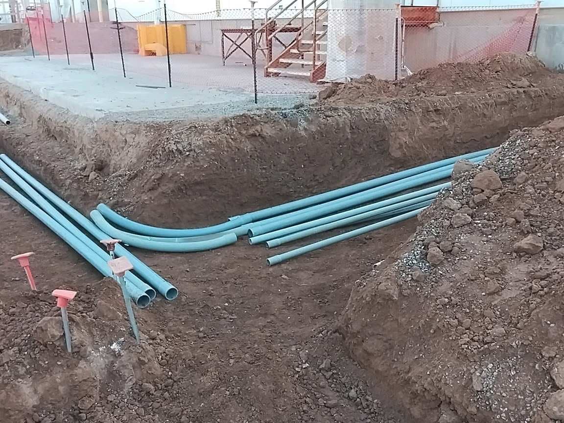 Open trench with several conduit runs sweeping toward a building